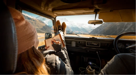 A woman in a Land Rover in New Zealand with her feet on the dashboard looking at mountains.
